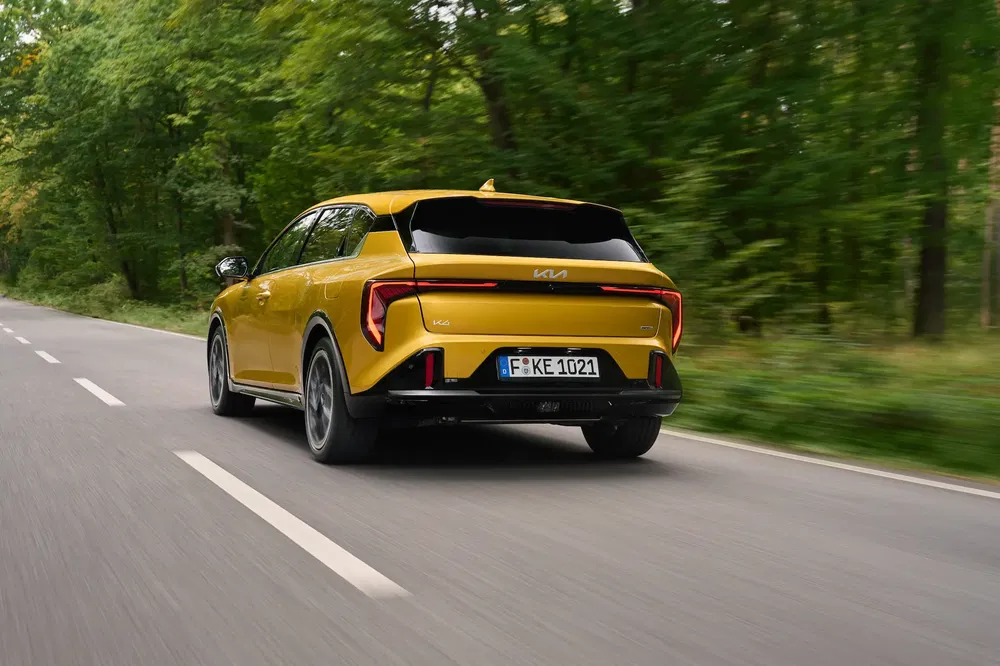 Gele Kia Ceed rijdt op een boomrijke weg, opvallend achterontwerp.