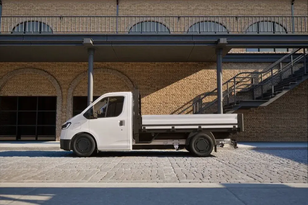 Witte lichte elektrische vrachtwagen geparkeerd voor een bakstenen gebouw.
