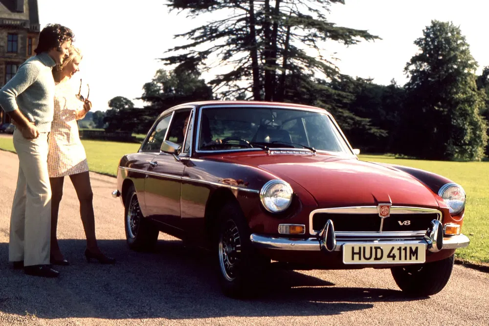 Couple admirant une MG B GT rouge des années 70 dans un parc verdoyant.