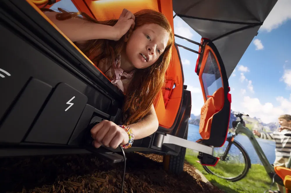 Jeune fille dans une voiture orange avec une prise de courant, vélo en arrière-plan.