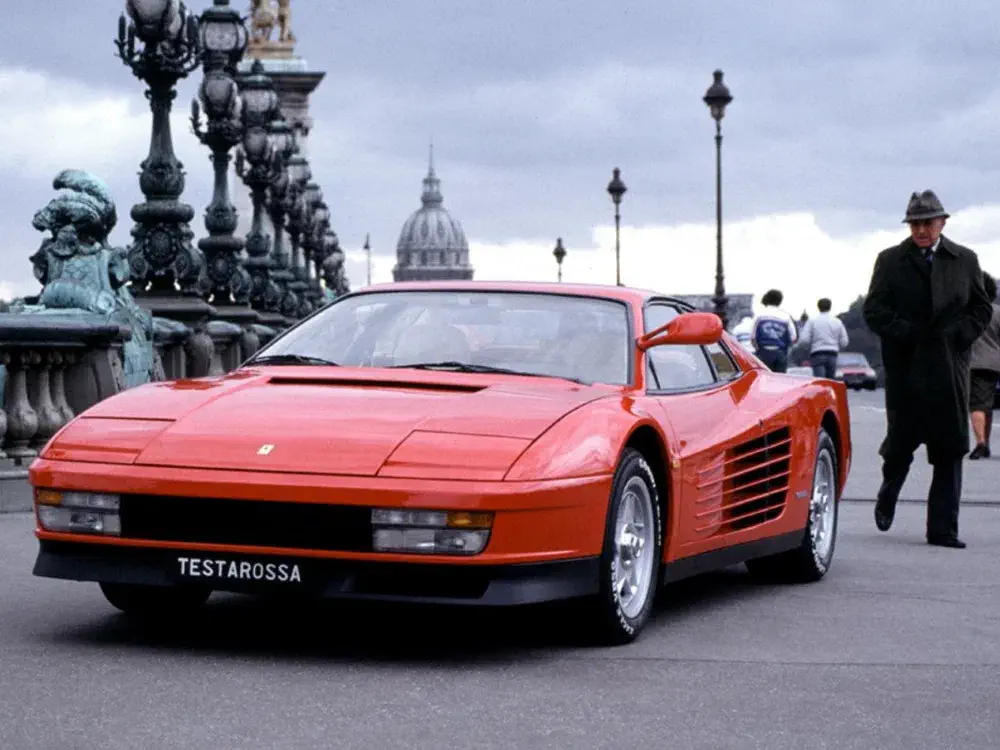 {"fr":"Ferrari Testarossa rouge sur un pont élégant avec une architecture classique en arrière-plan.","nl":"Rode Ferrari Testarossa op een elegante brug met klassieke architectuur op de achtergrond."}