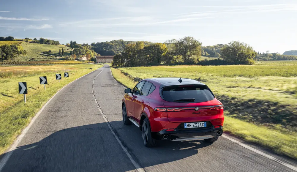 Alfa Romeo Tonale rouge conduit sur une route de campagne sinueuse et pittoresque.