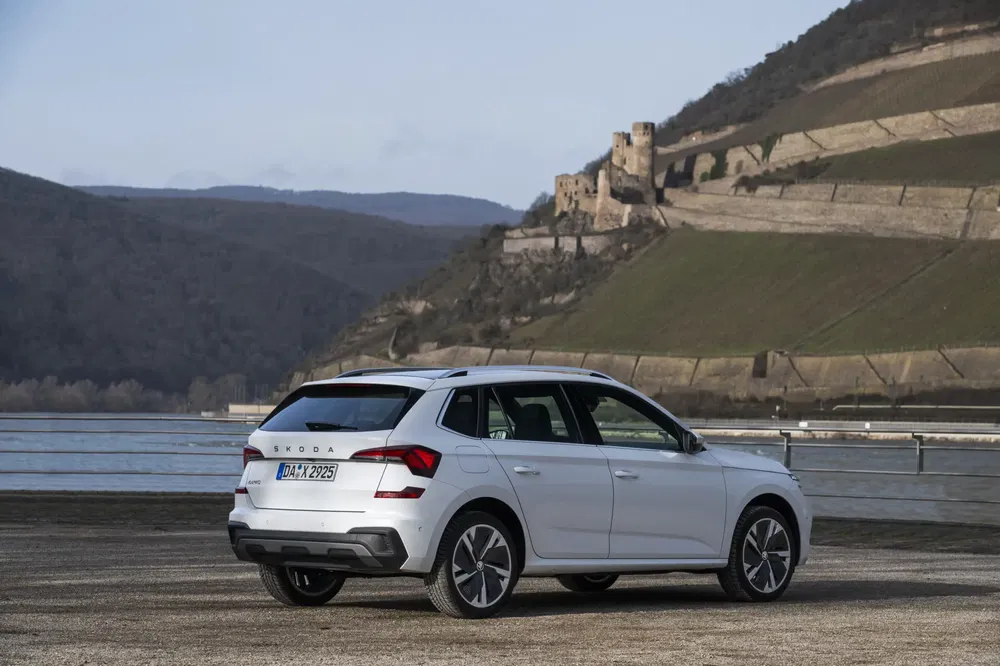 Witte Škoda SUV geparkeerd voor heuvelachtig landschap met oud kasteel op achtergrond.