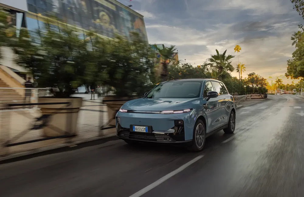 Moderne elektrische SUV BYD Tang rijdend op weg met palmbomen bij zonsondergang.