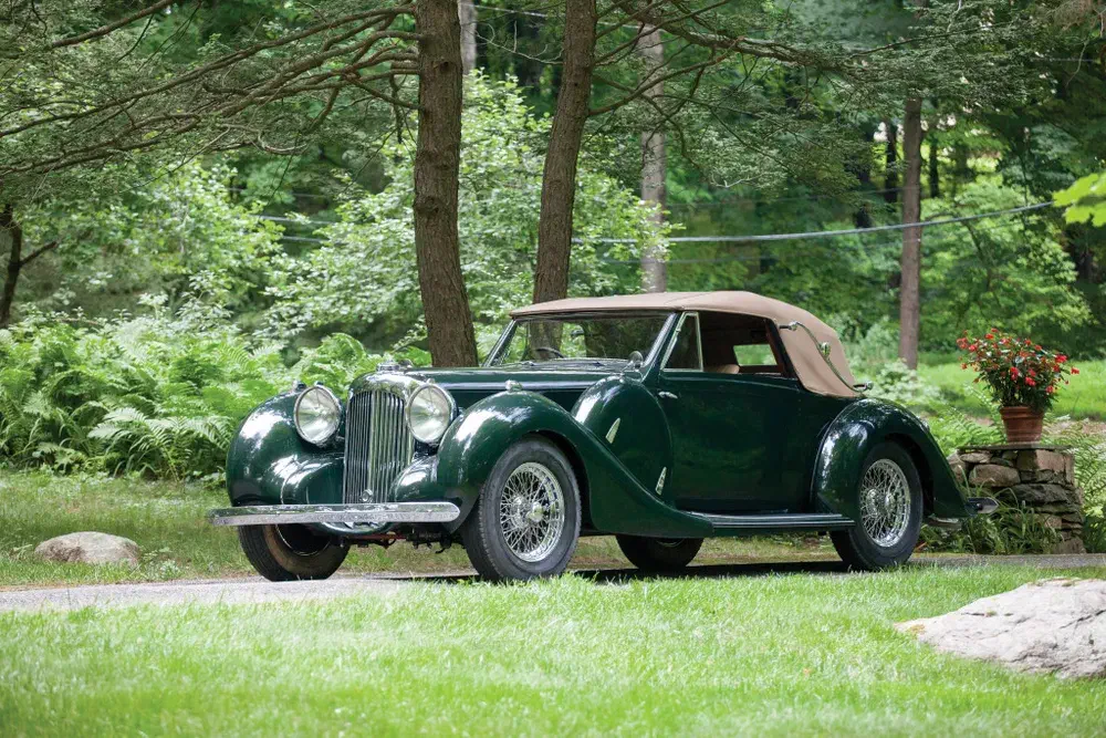 Voiture de collection Bentley verte dans un cadre forestier avec capote beige.