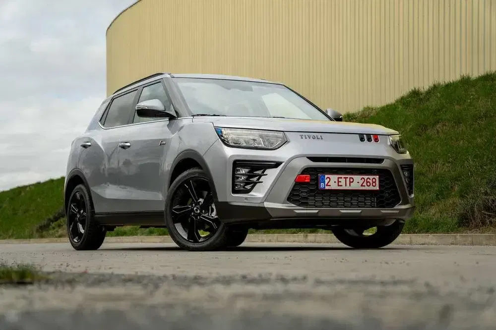SUV SsangYong Tivoli gris garé sur une route, avec plaque belge, arrière-plan industriel.