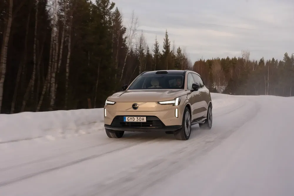 Volvo SUV beige roulant sur une route enneigée entourée de forêt hivernale.