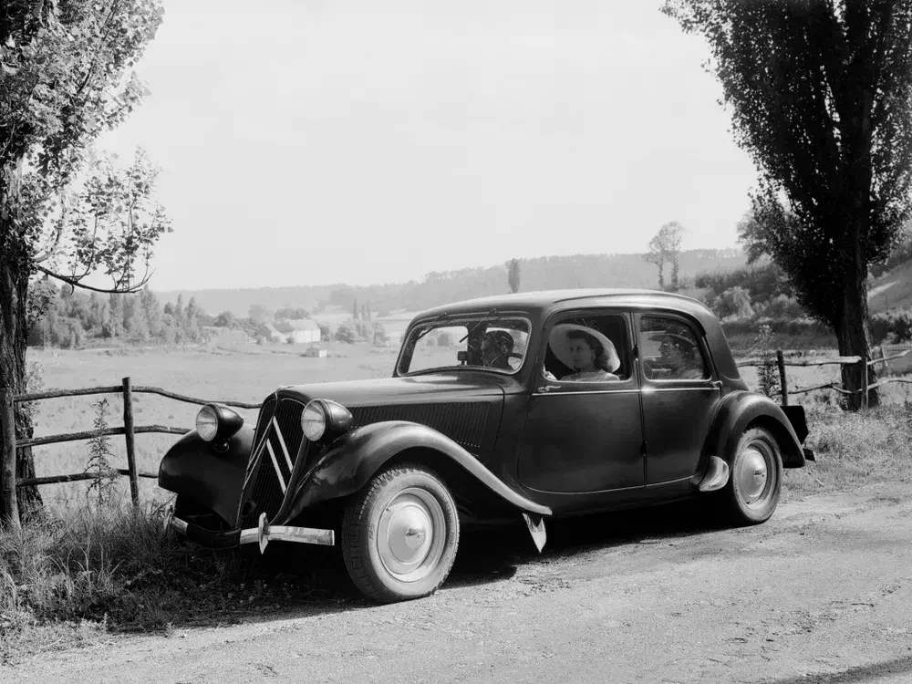 Citroën Traction Avant noire sur une route de campagne avec paysage champêtre.