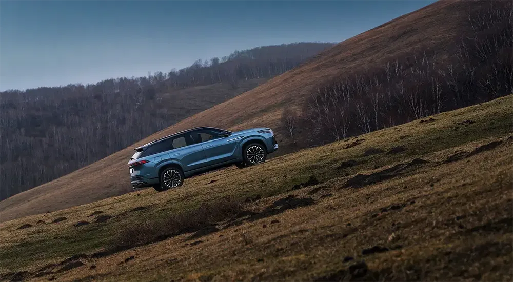 Blauwe SUV beklimt grasrijke heuvel met bos op achtergrond, off-road rijervaring.