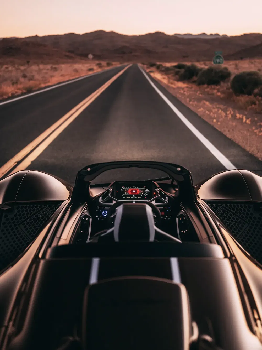 Vue intérieure d'une supercar sur autoroute désertique au crépuscule, affichage numérique allumé.