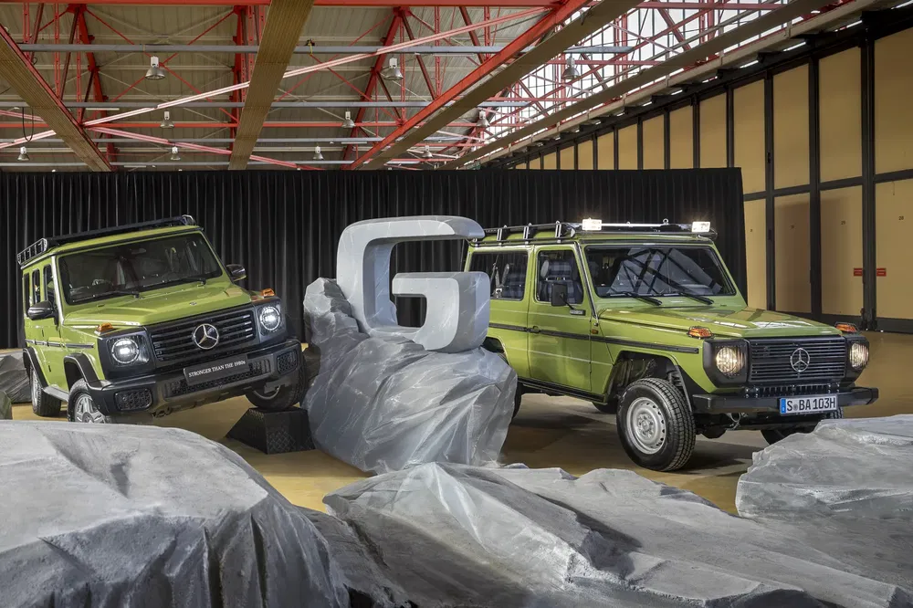 Twee groene Mercedes G-Klasse tentoongesteld in een hal met gestileerde rotsachtige achtergrond.