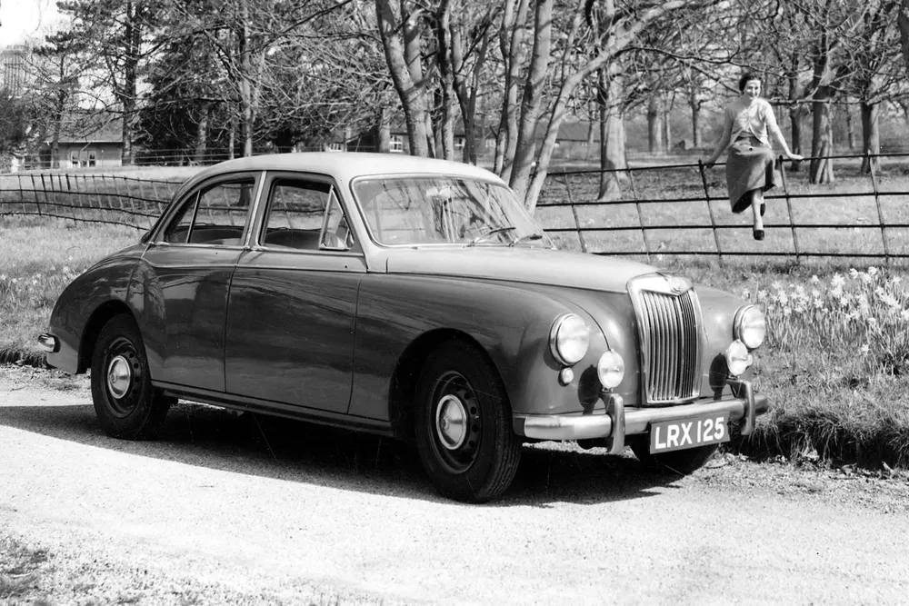 Voiture classique MG Magnette noire, parcée sur une route de campagne avec des arbres en arrière-plan.