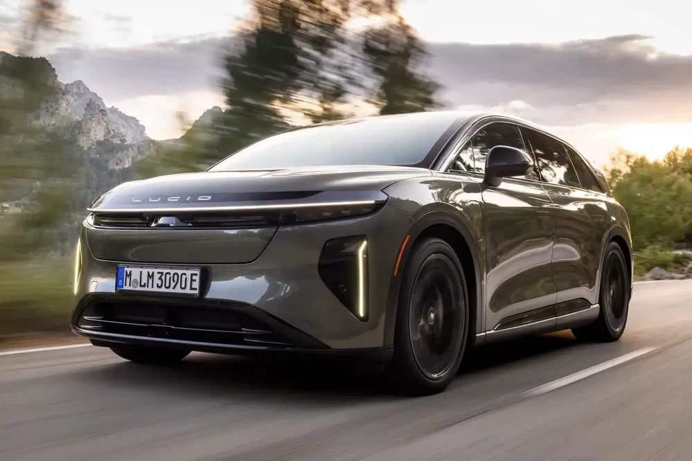 Voiture électrique Lucid Air roulant sur une route entourée de montagnes et de verdure.