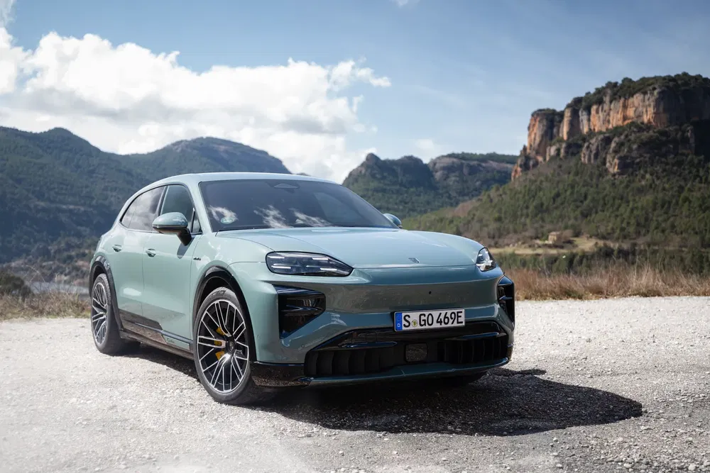 SUV électrique Porsche Macan couleur bleu-vert en pleine nature, montagnes en arrière-plan.
