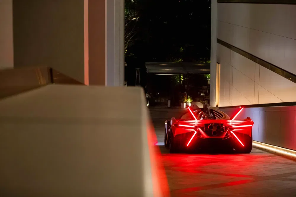 Futuristische sportwagen verlicht door rode neonlichten, geparkeerd in een donkere stadsomgeving.