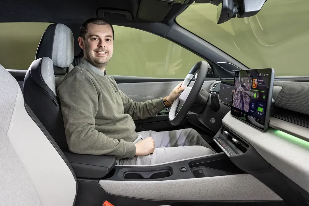 Homme souriant dans intérieur d'une voiture moderne avec écran tactile central.
