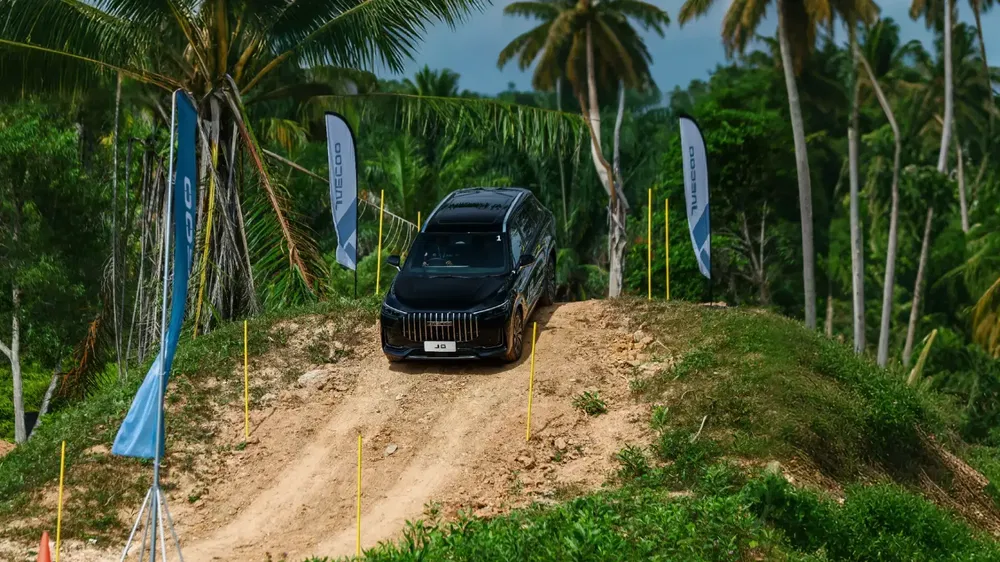 Chirey SUV op ruw terrein met palmbomen en reclamebanners, offroad prestaties.