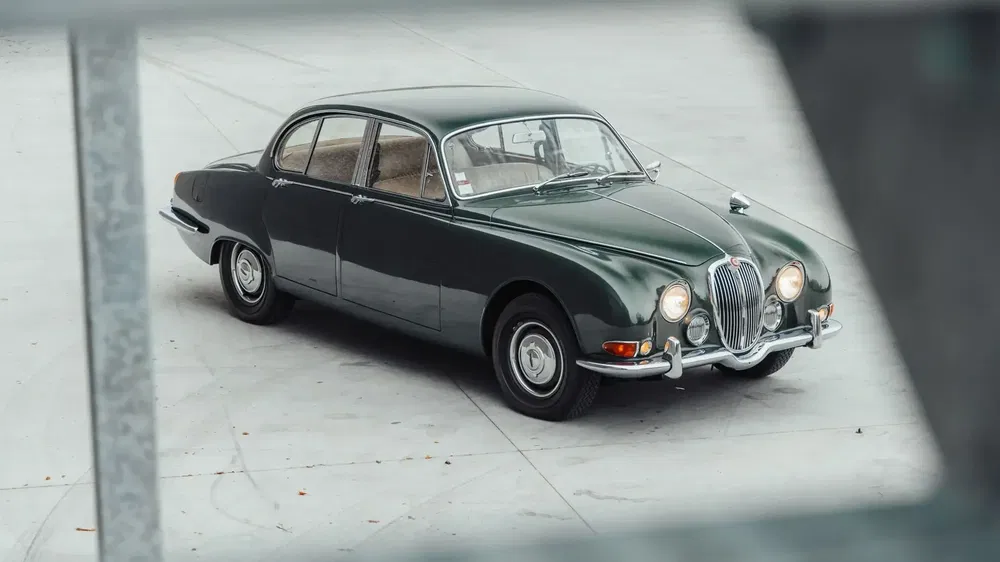 Jaguar Mark 2 classique vert sur parking, design élégant et intemporel.