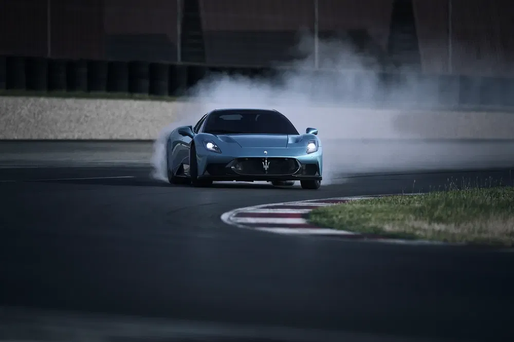 Blauwe Maserati MC20 driftend op circuit, rookwolken achter, scherpe bocht.