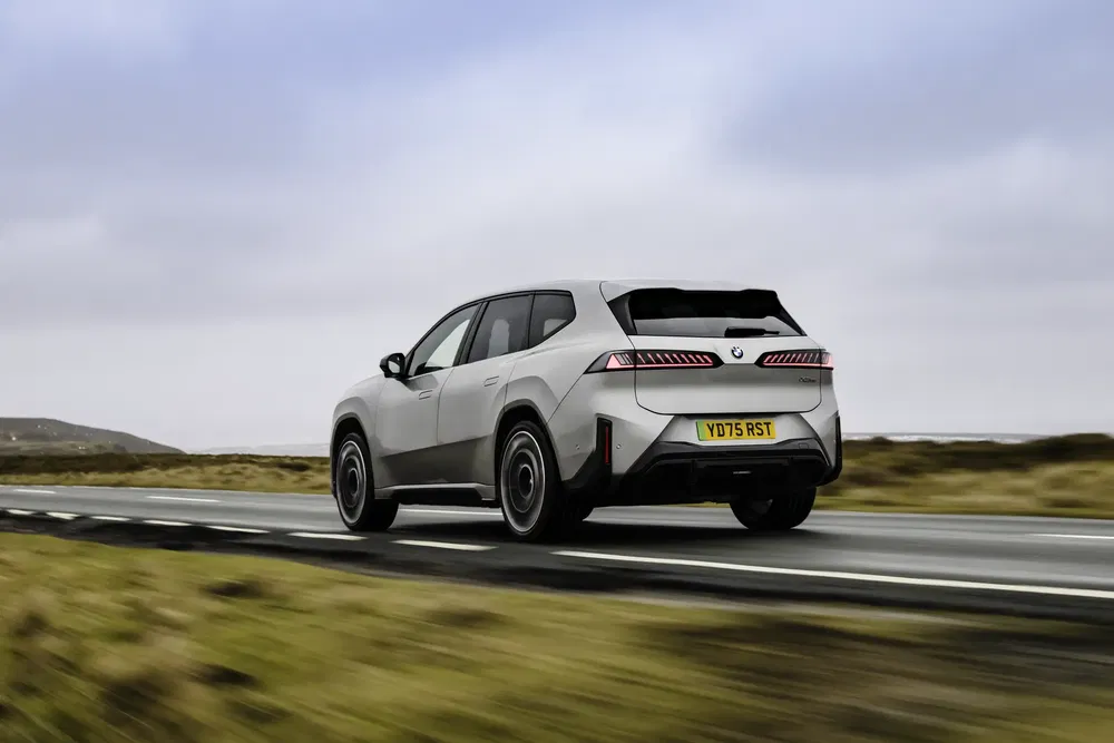 BMW iX roulant sur une route déserte avec ciel nuageux.
