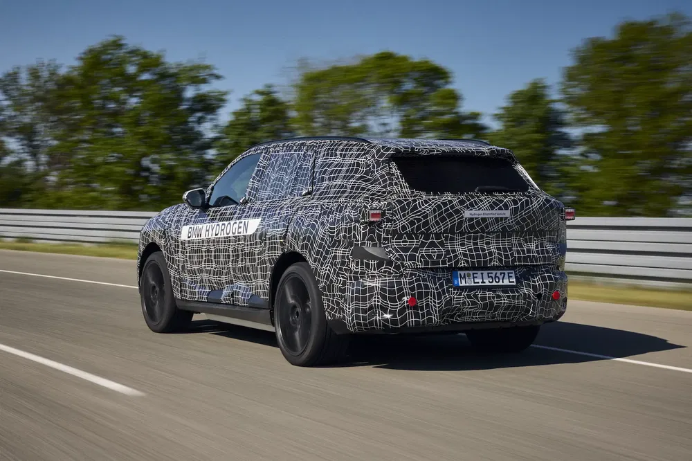 Prototype camouflé BMW iX5 Hydrogen sur une piste d'essai, forêt en arrière-plan.