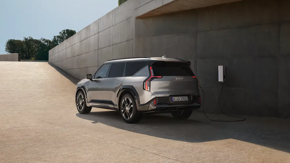 Kia EV9 électrique en recharge devant un mur minimaliste en béton.