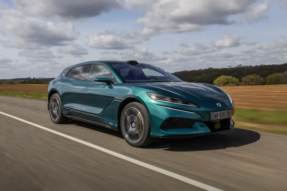 Voiture électrique Lotus Emeya verte sur une route de campagne par temps nuageux.