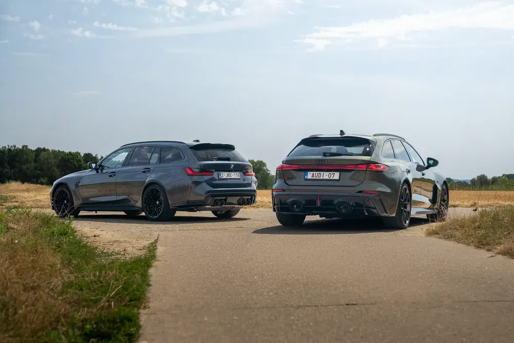 Twee sportieve stationwagens BMW M3 en Audi RS6 geparkeerd op een landweg.