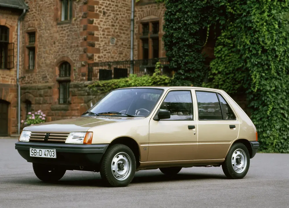 Peugeot 205 dorée stationnée devant un bâtiment en briques, années 80.