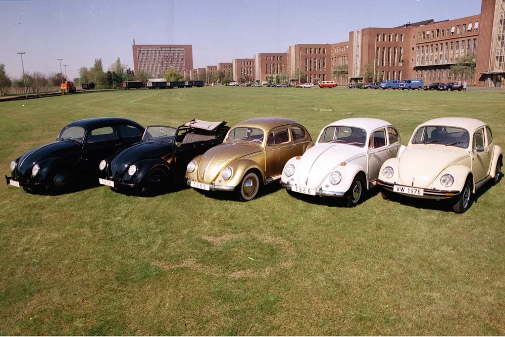 Cinq Volkswagen Coccinelle vintage alignées sur une pelouse verte devant des bâtiments historiques.