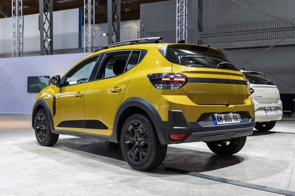 Gele Dacia Sandero in een showroom, gepresenteerd met een ander voertuig op de achtergrond.