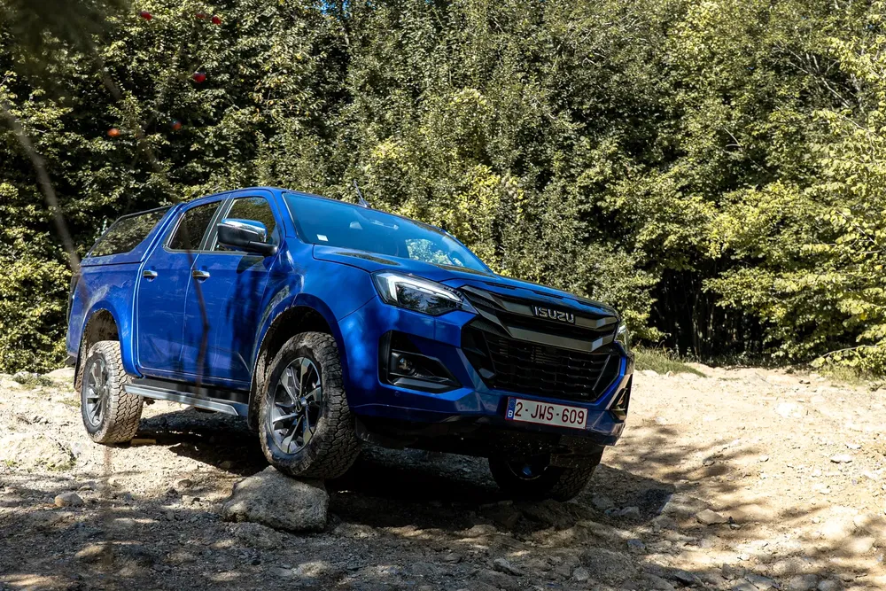 Isuzu D-Max bleu naviguant un sentier rocheux en forêt, démontrant ses capacités tout-terrain.