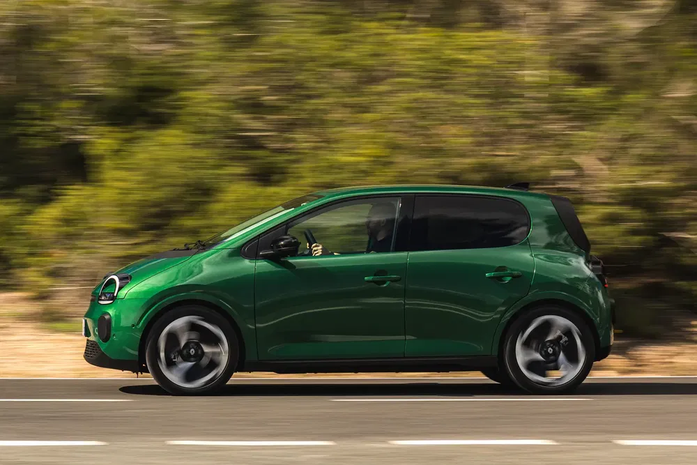 Voiture compacte VW e-Up verte roulant sur une route, profil latéral en mouvement.