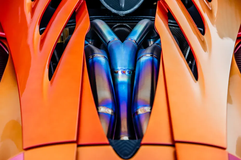 Oranje sportwagen motorkap met zichtbaar complex metalen uitlaatsysteem.