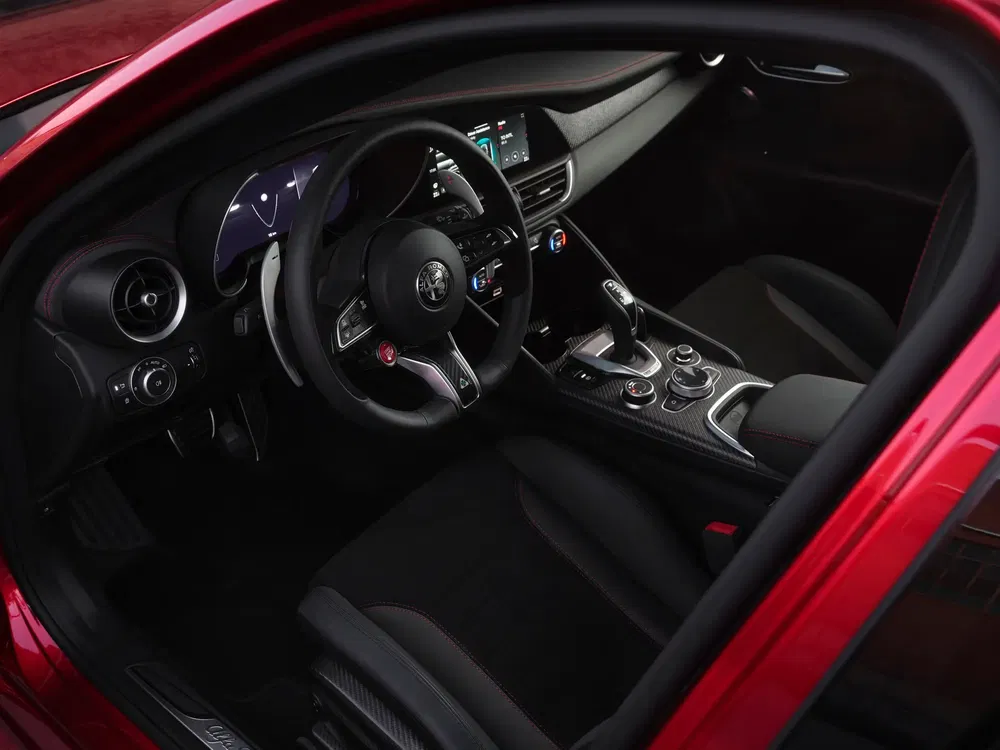 Interieur van een Alfa Romeo met modern dashboard en sportief lederen stuur.