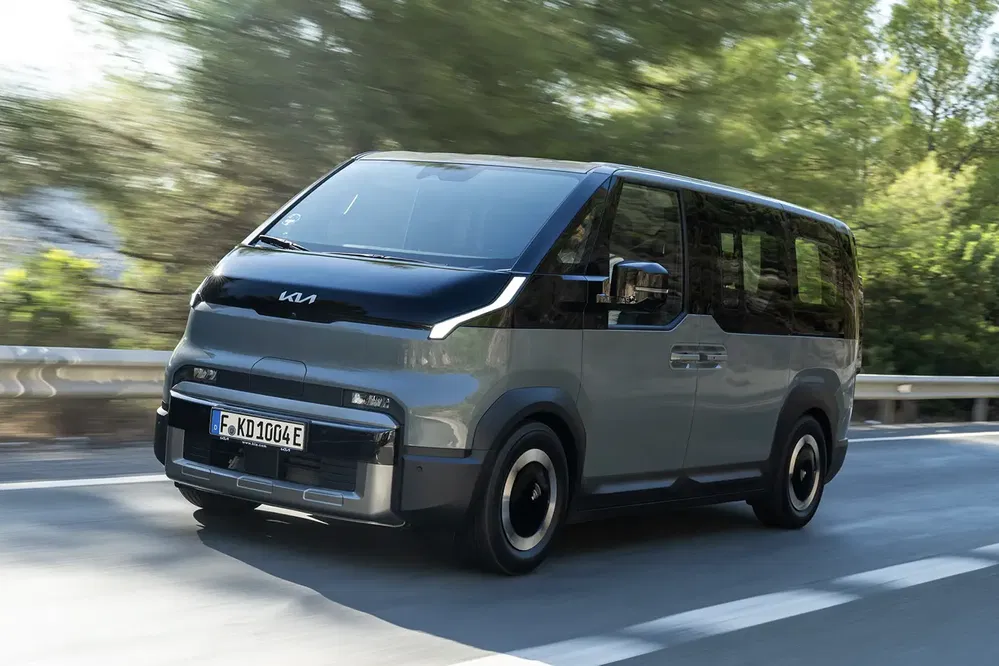 Kia EV9 minivan roulant sur route bordée d'arbres, design moderne et aérodynamique.