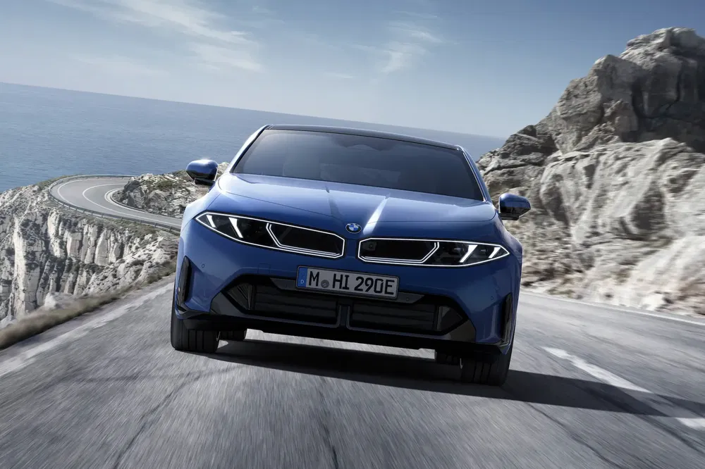 BMW électrique bleu conduisant sur route côtière sinueuse, paysage rocheux spectaculaire.