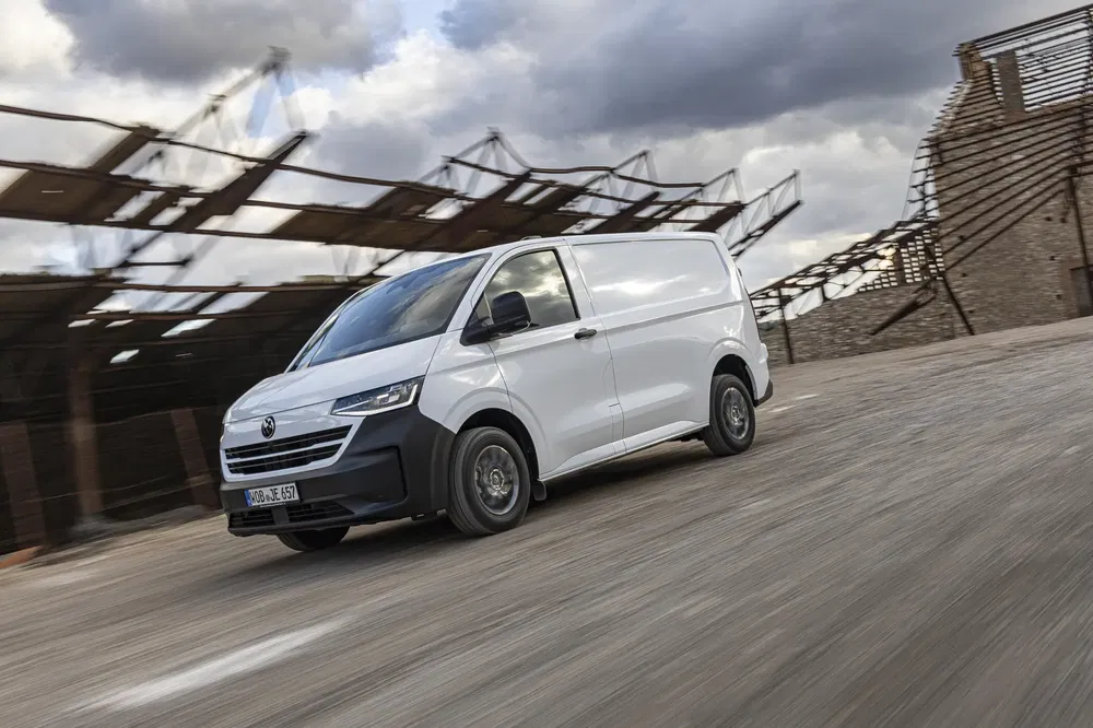 Witte Volkswagen Transporter rijdt op de weg met bewolkte lucht op de achtergrond.