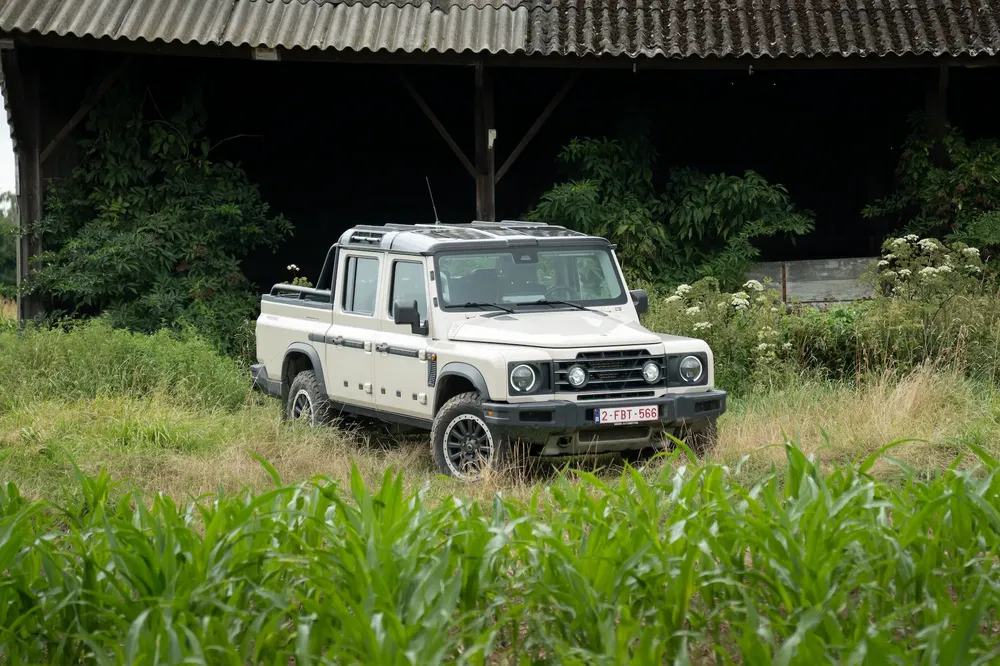Vintage Toyota Land Cruiser geparkeerd bij een schuur, omgeven door weelderige vegetatie.