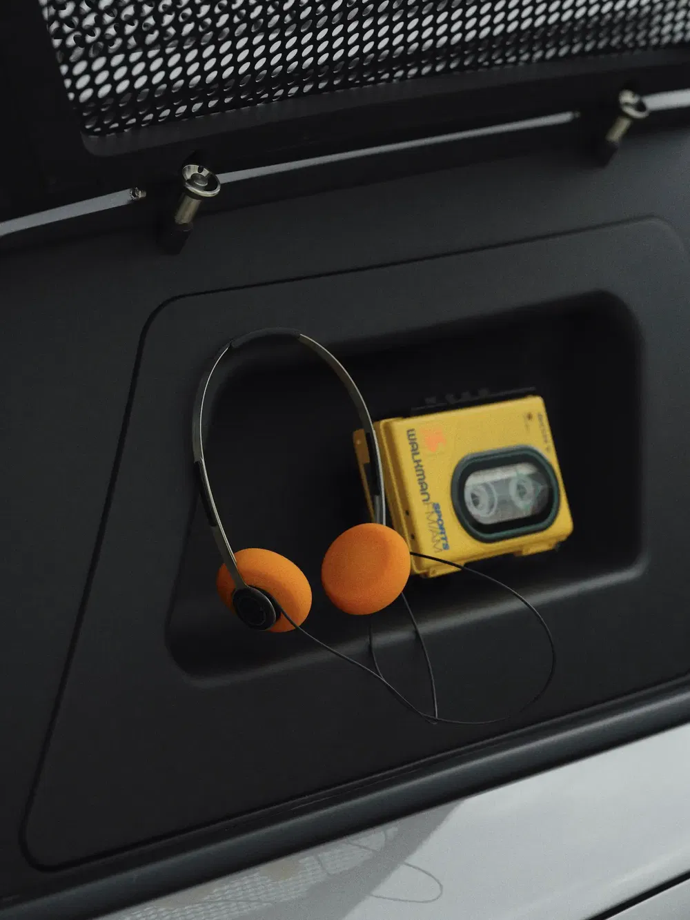 Casque orange rétro et Walkman jaune dans le coffre d'une Porsche.