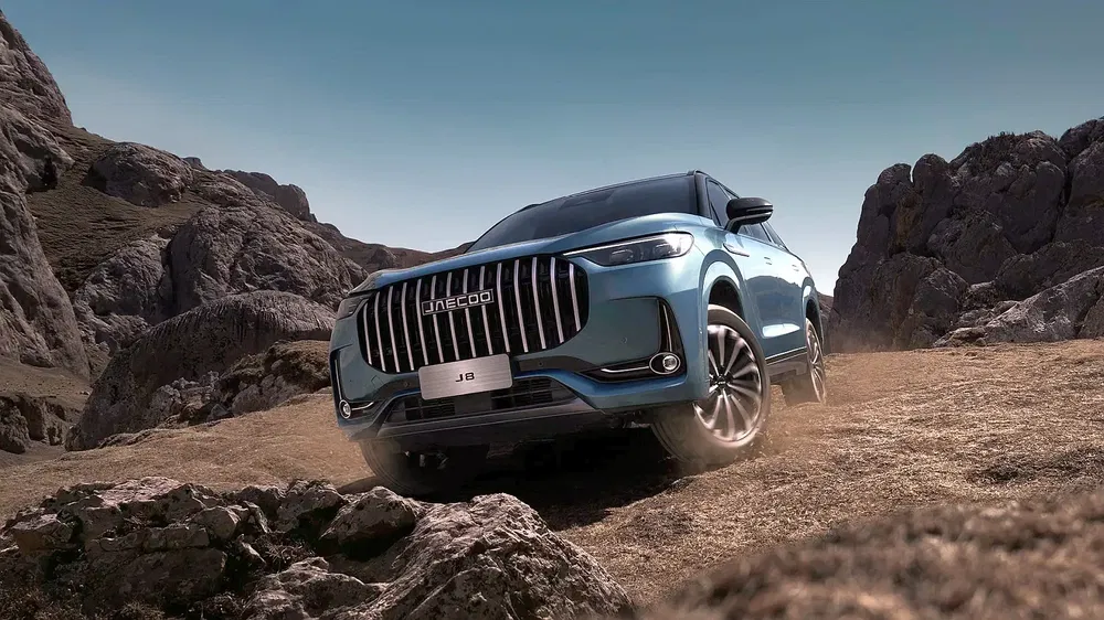 Blauwe Jaecoo J8 SUV op bergachtig terrein, opvallend voorrooster en robuust ontwerp.