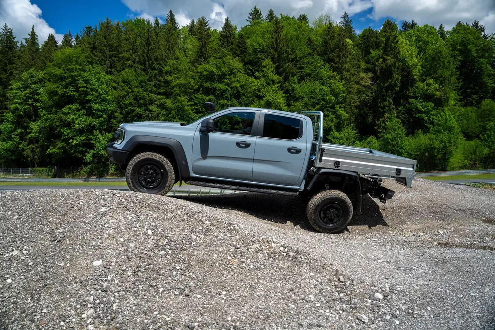 Pick-up Volkswagen Amarok traversant terrain rocheux, forêt dense en arrière-plan.