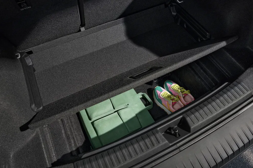 Compartiment de rangement sous plancher avec chaussures et sac vert dans un coffre de voiture.