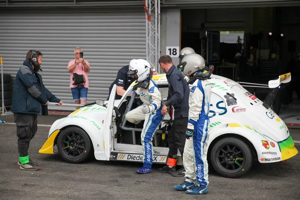 Rijders stappen in VW Fun Cup raceauto op circuit, begeleid door monteurs.