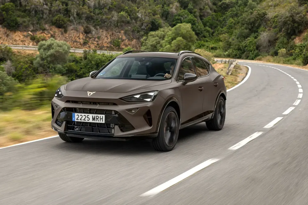 Bruine elektrische Cupra Tavascan op een kronkelende weg omgeven door groen.