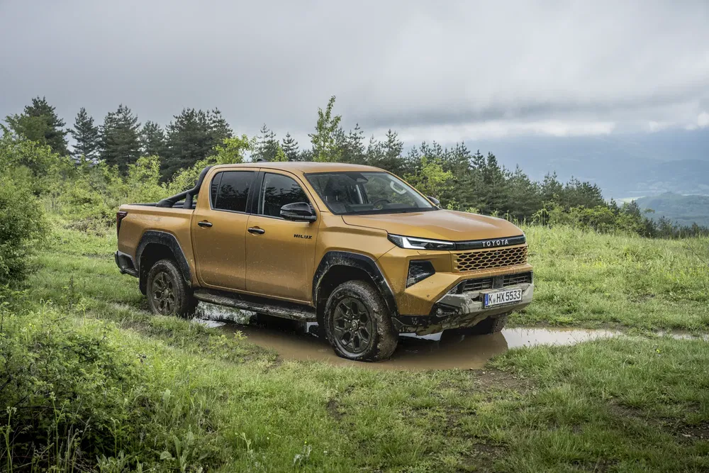 Toyota Hilux Revo GR Sport couleur bronze roulant sur terrain boueux en pleine nature.
