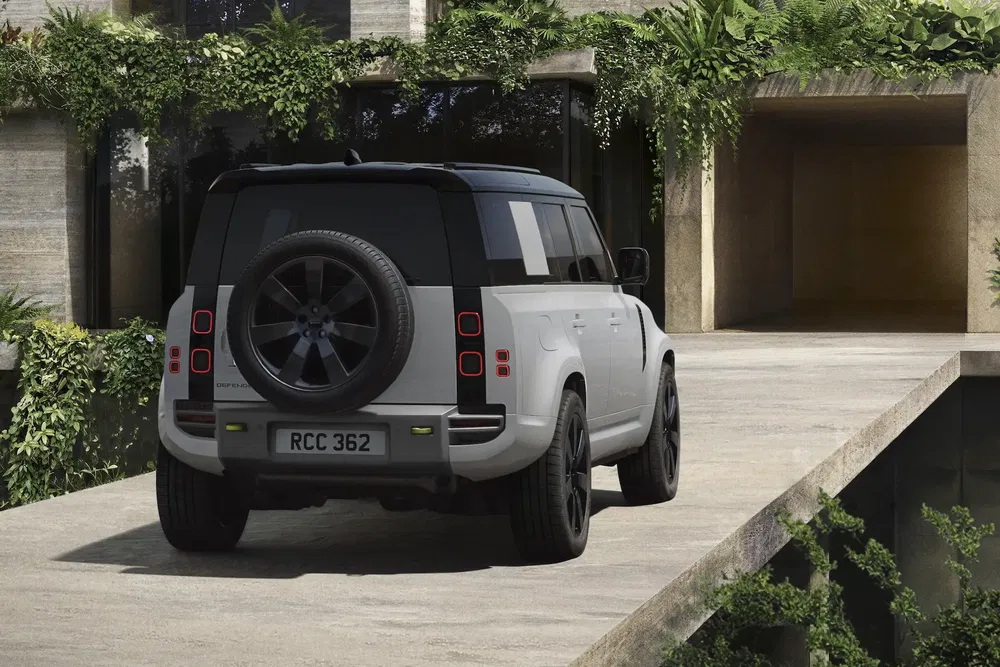 Land Rover Defender garé devant une maison moderne, entouré de verdure luxuriante.