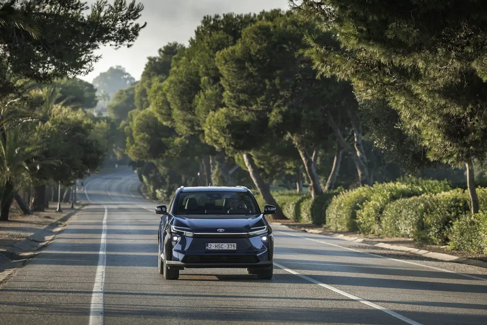 De Hyundai Ioniq 5 rijdt op een met bomen omzoomde weg op een zonnige dag.