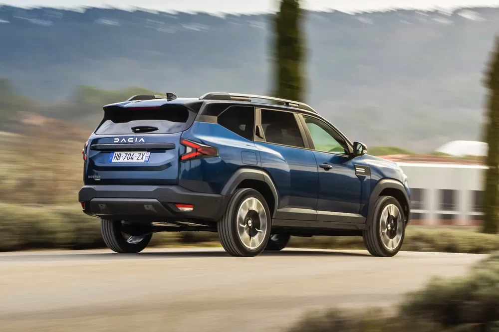 Dacia Jogger SUV rijdt in landelijke omgeving, zicht van achteren, blauwe metallic kleur.