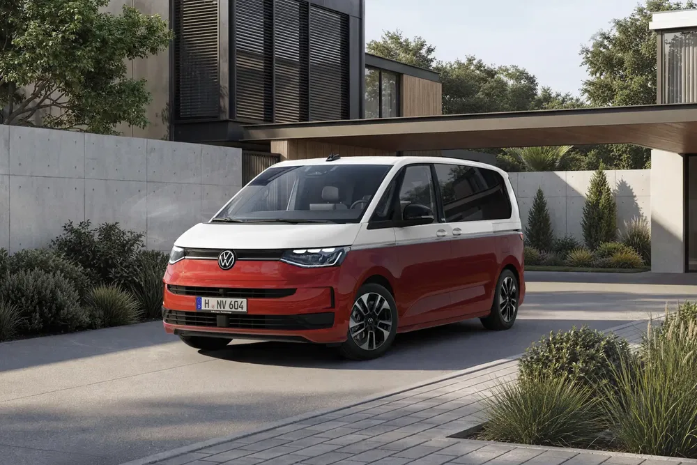Volkswagen Multivan rouge et blanc garée devant une maison moderne avec jardin.